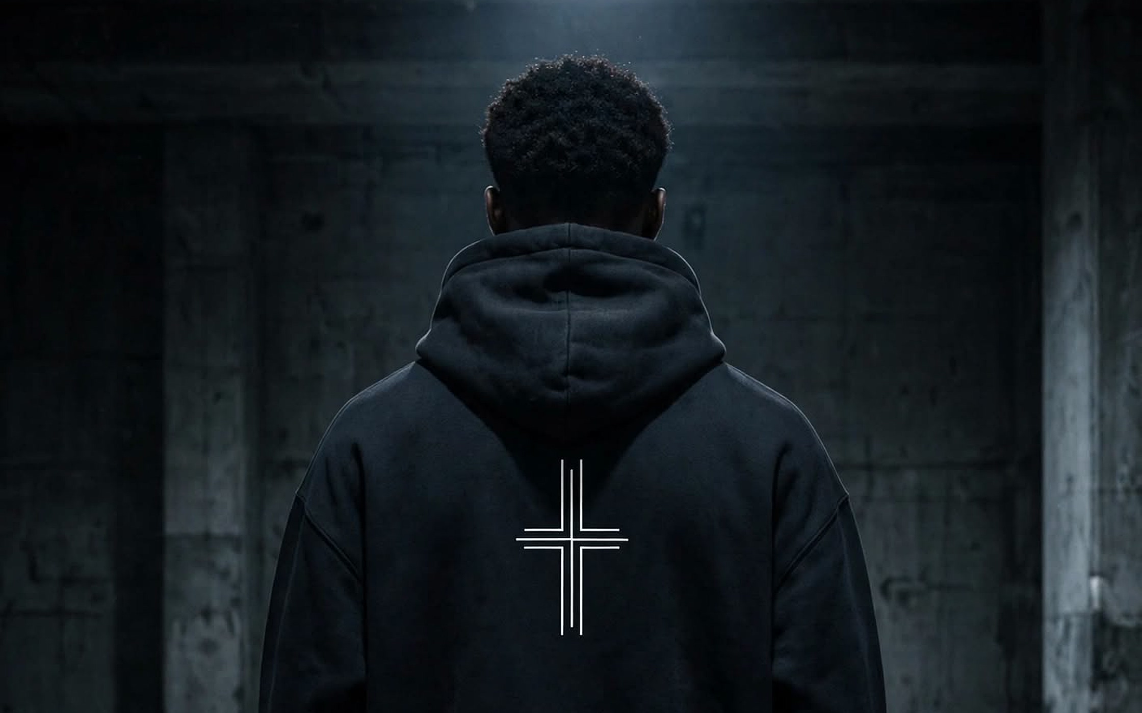 Back of the black Cross Hoodie under a single overhead light